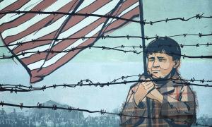 Child holding US flag behind barbwire