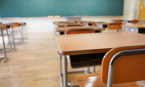 Empty desks in a classroom with a blackboard in the background.