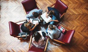 Group of people gathered around in a circle looking at various materials in front of them.