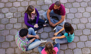 A group of teens sits in a circle having a conversation. 