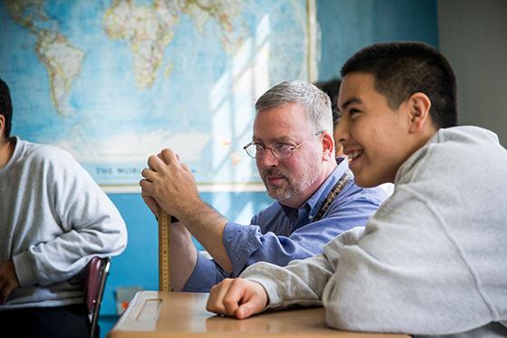 A teacher looks on and a student laughs