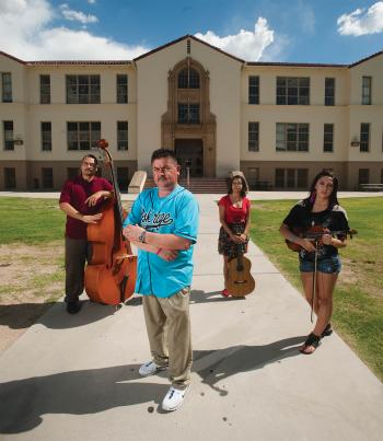 four people standing in front of building holding string instruments