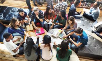 Several older students in discussion with each other, gathered around two tables with open books on them.