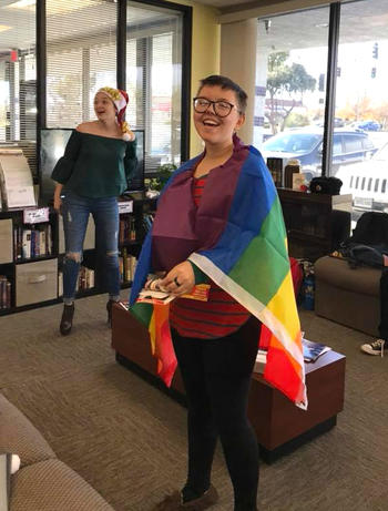 Young smiling student with the rainbow flag draped over their shoulders.